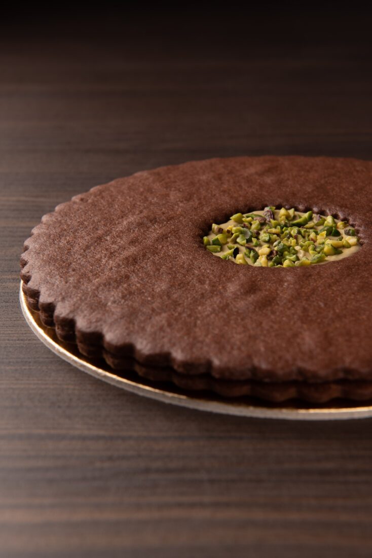 Artisan chocolate tart with creamy center and chopped pistachio topping, professional food photography.