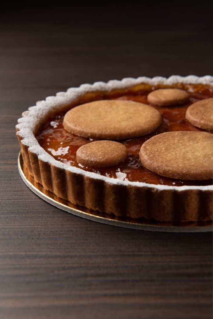 Close-up of artisan tart with peach jam and circular pastry decorations on a wooden background, food photography Vicenza.