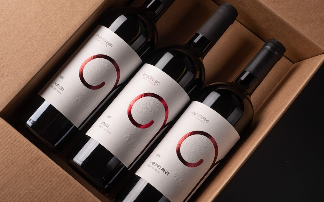 Three Fondo Rubro red wine bottles arranged in a cardboard box, professional still life photography in Italy.