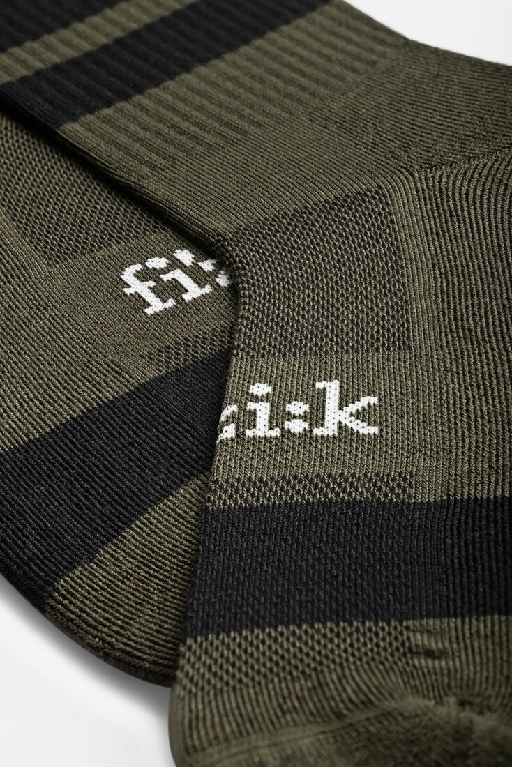 Dettaglio macro di calze tecniche da ciclismo Fizik a righe verde oliva e nere con logo ricamato.