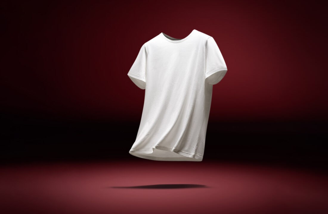 T-shirt bianca in cotone fluttuante su sfondo rosso scuro, fotografia professionale di abbigliamento e-commerce.