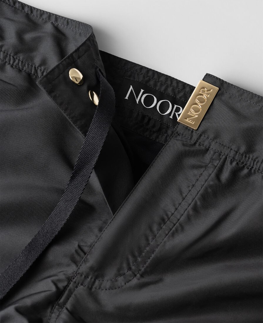 Detail of the Noor logo on black swim shorts, photographed in Italy by Inlet Studio in a professional photoshoot.